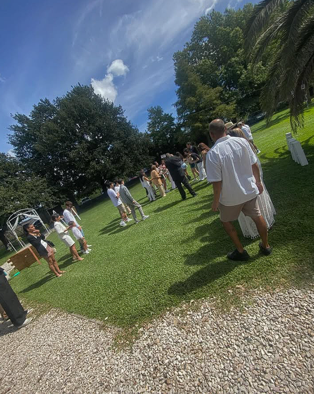Invitados con vestidos, camisas y bermudas en una celebración al aire libre